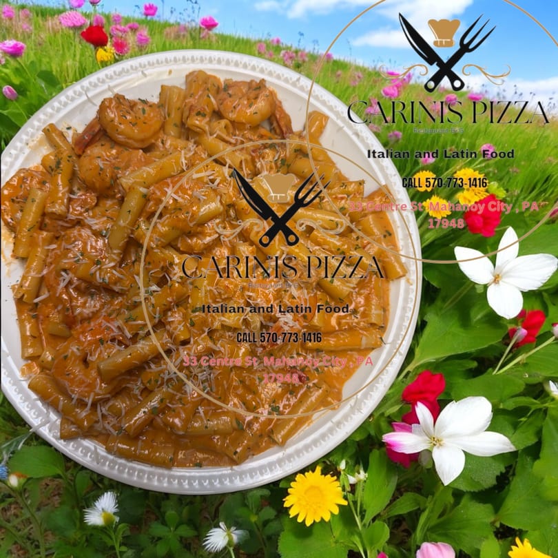 Pasta with shrimp in a creamy sauce, topped with cheese and herbs, on a plate surrounded by colorful flowers.